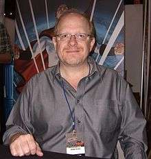 Waid looking toward the camera and smiling in front of an Irredeemable poster