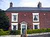 A brick house with four sash windows and a green front door.