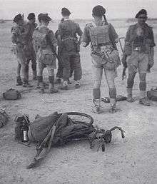 Seven British soldiers only one facing the camera, wearing hot climate uniform in a desert terrain