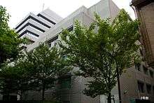 Large grey building, surrounded by young trees