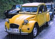 A yellow car drives down a grassy road.