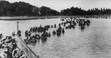 British soldiers wading ashore from landing craft, in the background is a tree lined beach