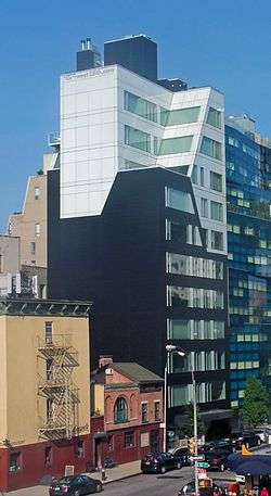 A black and white high-rise building on a city street with a smaller one in front and a larger one behind it. The boundaries between the two colors on the building's face are irregularly shaped, near its upper stories