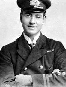 Head-and-chest portrait of smiling man with folded arms, wearing dark-coloured uniform and peaked cap.