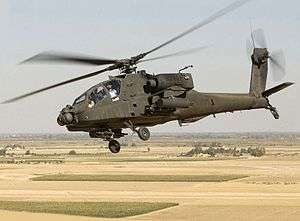 Photo of tilted horizon showing helicopter flying above barren land with rectangular patches of green grass.