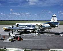 A white and blue aeroplane on a runway, surrounded by tankers of fuel and other equipment. The tail bears a stylised red Zimbabwe Bird, and the words "AIR RHODESIA" are painted above the windows of the cabin. Towards the rear are painted the letters "YP-YNC", with the green and white Rhodesian flag rendered above.