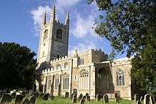 A stone church seen from the southeast with Perpendicular windows, embattled parapets, and a west tower with tall pinnacles