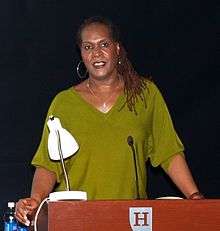 A black woman in a green top speaks from behind a wooden podium that reads "Hamline University".