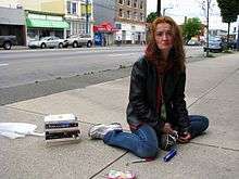 Photograph of a woman with facial lesions, sitting on the sidewalk