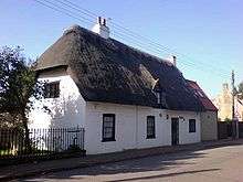 White thatched cottage single storey 3 windows 1 front door 1 attic window chimney No front garden