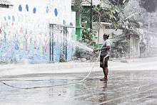 A man holding a hose and spraying volcanic ash with water