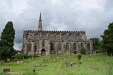 A stone church seen from the south with multiple large windows in the south aisle and clerestory, a two-storey south porch, and part of the spire beyond