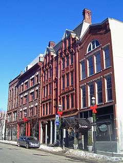 Four attached brick buildings with different styles of decoration viewed from across a city street