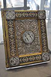 Gilt and enamelled Bible cover richly decorated with foliage and flower motifs. In the centre there is a round boss depicting Christ surrounded by two angels. Each corner contains a square boss, each showing a representation of Matthew, Mark, Luke or John.