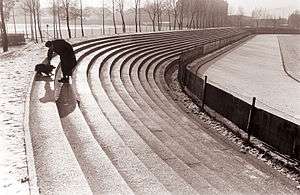 Black and white photograph of a man and his dog who are playing on the concrete terraces of the Ljudski vrt.