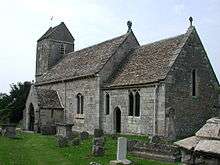 A stone church seen from the southeast, showing the chancel, beyond which is a nave with a higher roof and a porch and, beyond that, a tower with a saddleback roof