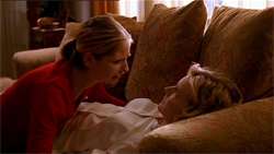 A woman cries as she kneels over her mother, who is lying dead on a sofa.