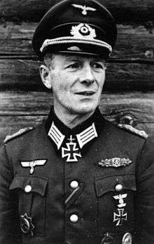 A man wearing a military uniform and peaked cap with an Iron Cross displayed at the front of his uniform collar.