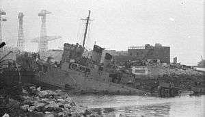 ship at 45 degree angle showing damage caused by German gunfire and impact with the dock