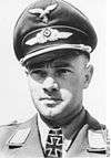 A man wearing a peaked cap and military uniform with an Iron Cross displayed at the front of his uniform collar.