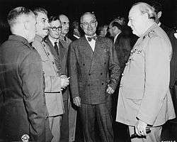 Three men in suits standing with several men in the background