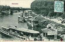 A black and white photograph of a quayside, showing several boats with passengers boarding and disembarking.