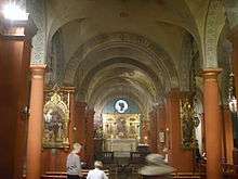 A view down the nave towards the altar. Smooth red columns support cream arches with grey-blue floral decorations. There is a round window above the altar.