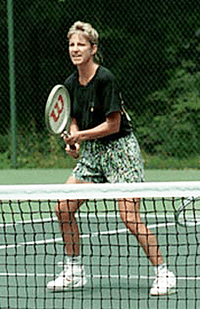 A blonde-haired female tennis player with multi-colored shorts and a black shirt, with the tennis racket out in front of her