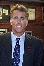 A middle-aged man, wearing a dark blazer, light-coloured shirt, and a blue and white tie.