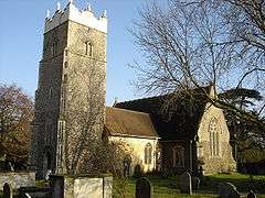 A stone church seen from the southwest.  Nearest is the tower with a battlemented parapet bearing statues, then a short nave, and a larger south transept