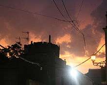 Coria sunset after rain.  Sun is setting behind black silhouette of castle; and it lights heavy dark clouds from below