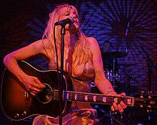 Woman in dress playing acoustic guitar and signing in microphone