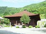 Wooden building with a hipped roof and an enclosing veranda without handrails.