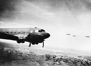 Four twin-propeller aircraft fly over a mountain range