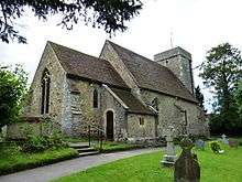 A photograph of a small church with a steep v-shaped roof and square tower at the far end