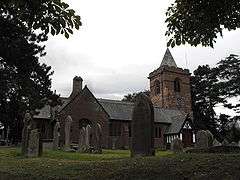 A church seen from the north; to the right is a tower with a small pyramidal spire; projecting from the church are a gabled transept and a timber-framed porch. In the foreground are gravestones