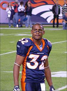 An American football player looks at the crowd. He is wearing his uniform on the field with some spectators in the background.