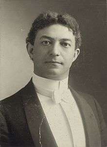 Black and white portrait of a white man with dark hair. He is wearing a tuxedo with a white bow tie.