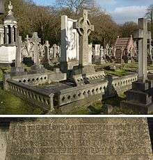 A granite headstone surmounted by a tall, granite Celtic cross, among several other gravestones