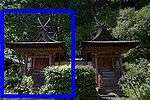 A small wooden building next to another identical building with gabled roof, a stair on the gable side covered by an extended roof. The roof ridge has forked finials.