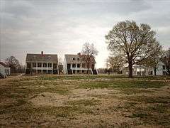 Photograph of the parade ground and surrounding, two-story, white, Army buildings in the early spring.