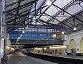 The interior of a building with white walls, white flooring, and a railway track running down the middle of the corridor with a train on it