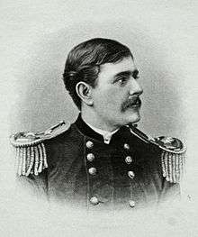 Head and shoulders of a white man with dark hair and a mustache, wearing a double-breasted military jacket with fringed shoulder boards.