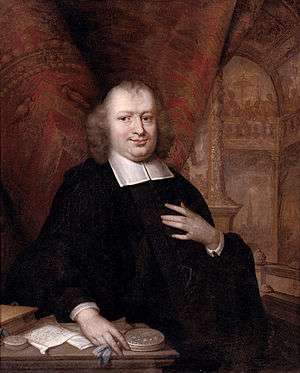 portrait of a plump man standing at a desk with papers lying on it