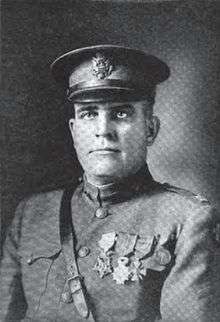 Head and shoulders of a middle-aged man in military uniform with a strap across his chest, four medals on his left breast, and a peaked cap.