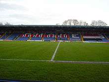 Bury F.C.'s blue stadium seated stand covered in red, white and black F.C. United banners.