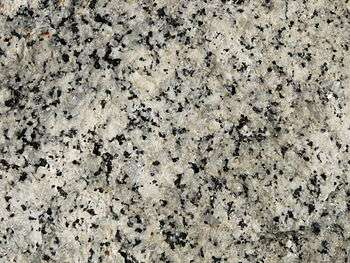 A closeup of the polished face of a slab of granite showing grains of white, bluish gray and black.