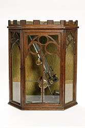 A stand microscope created by Joseph Gutteridge, a weaver from Coventry. The microscope allows coarse and fine adjustments, and its height is adjustable by a set screw. It consists of two objectives each with a screw on cap and a slidecarrier that is moveable laterally. The mirror also has a cap. It has a bench magnifier, lens moveable through 360° and has a base weighted with lead. It is placed in a Mahogany box containing seventeen six-compartment trays of slides.