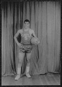 A man, wearing a jersey with a word "TEMPLE" and the number "5" written in the front, is holding a basketball while posing for a photo