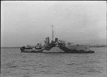 ship at sea steaming from left to right, her guns are unmanned and the bridge crew can be seen